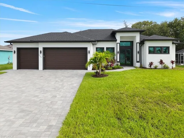 Prairie-style house with stucco siding, decorative driveway, a front lawn, an attached garage, and french doors