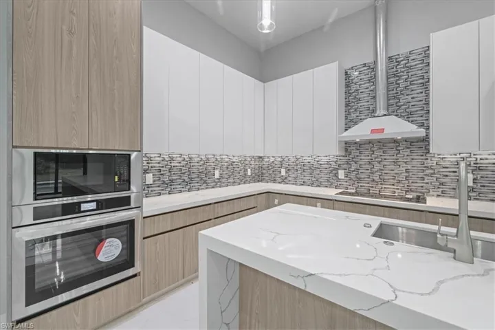 Kitchen featuring oven, modern cabinets, light stone countertops, and tasteful backsplash