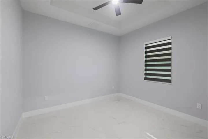 Unfurnished room with marble look tiles, a ceiling fan, and a raised ceiling