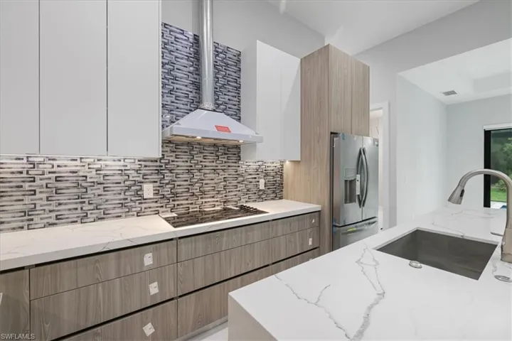 Kitchen featuring stainless steel fridge, modern cabinets, light stone counters, backsplash, and black cooktop