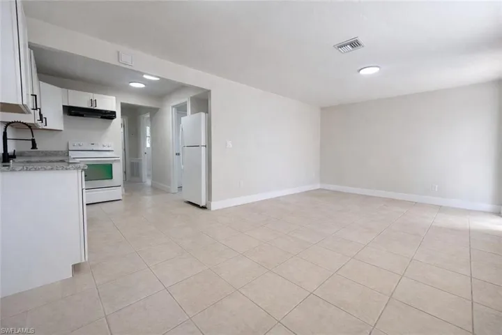 Kitchen with white appliances, white cabinets, light stone counters, under cabinet range hood, and light tile patterned flooring