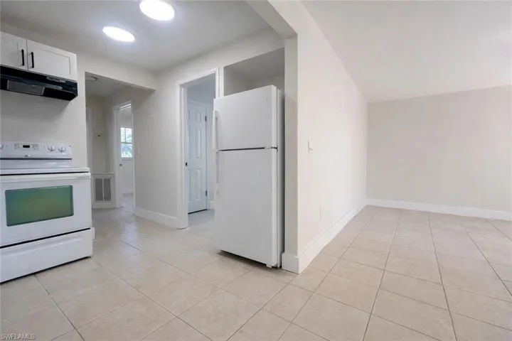 Kitchen featuring white appliances, under cabinet range hood, light tile patterned floors, and white cabinets