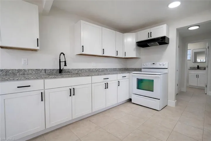 Kitchen featuring electric range, white cabinets, under cabinet range hood, light stone counters, and light tile patterned floors