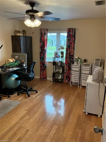 Room featuring wood-finish flooring, a ceiling fan with integrated lighting, and a window with blinds