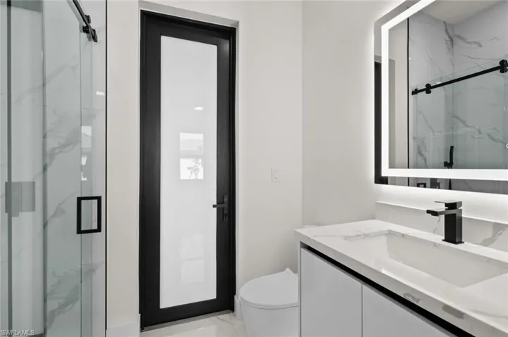 Full bath with marble look tiles, vanity, toilet, and a marble finish shower