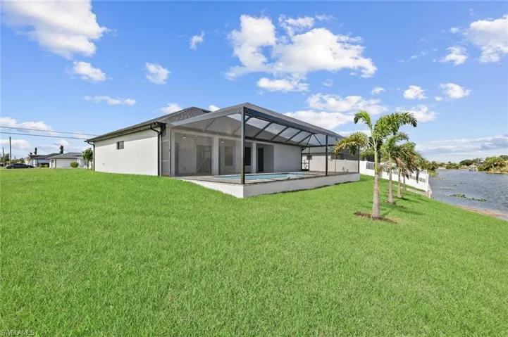 Rear view of property featuring a lawn, a water view, a lanai, and an outdoor pool