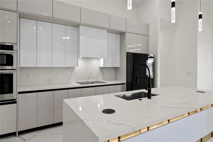 Kitchen featuring modern cabinets, black appliances, a sink, light marble finish flooring, and white cabinetry