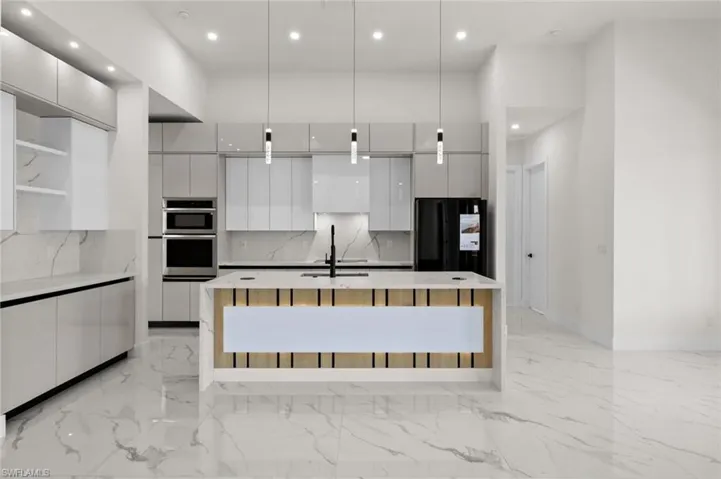 Kitchen featuring modern cabinets, freestanding refrigerator, white cabinets, recessed lighting, and a kitchen island with sink