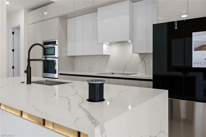 Kitchen featuring modern cabinets, white cabinetry, a sink, backsplash, and light stone countertops