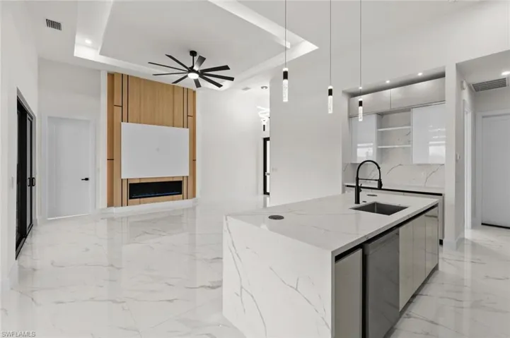 Kitchen with modern cabinets, a sink, a raised ceiling, light marble finish floors, and recessed lighting