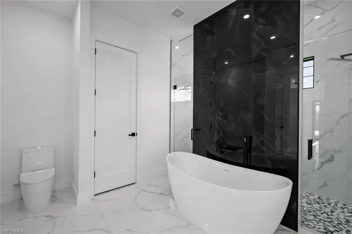 Full bath featuring marble tiled flooring, a freestanding bath, toilet, a marble finish shower, and baseboards