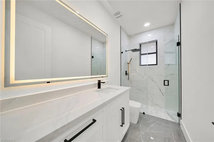 Bathroom featuring vanity, a marble finish shower, recessed lighting, and light marble finish flooring