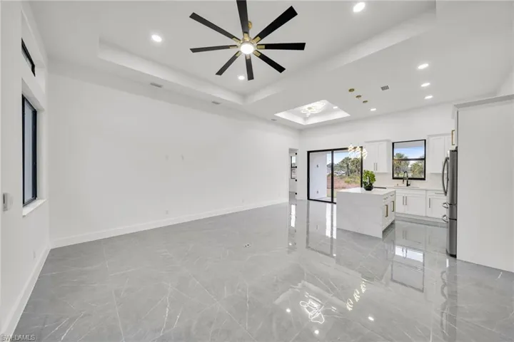 Unfurnished living room with light marble finish floors, a tray ceiling, a skylight, recessed lighting, and ceiling fan