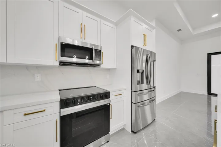 Kitchen with appliances with stainless steel finishes, white cabinets, light stone countertops, light marble finish floors, and recessed lighting