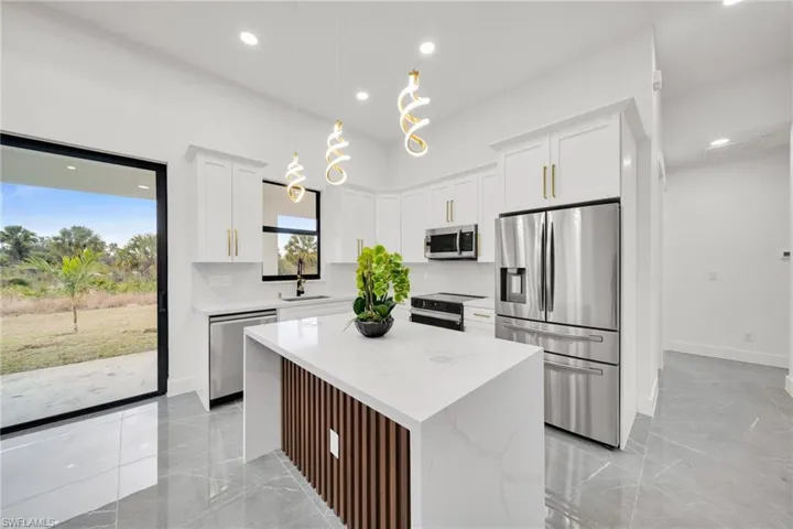 Kitchen with appliances with stainless steel finishes, white cabinets, a kitchen island, decorative light fixtures, and light stone countertops