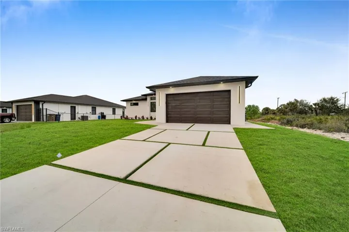 Prairie-style home featuring a front lawn, driveway, an attached garage, and stucco siding