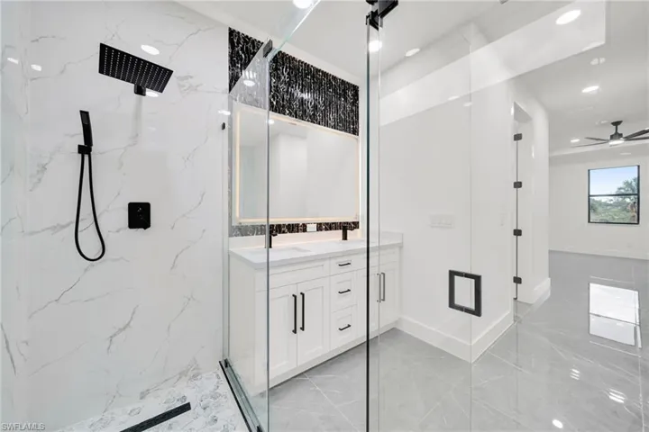 Full bathroom with double vanity, a marble finish shower, ceiling fan, recessed lighting, and light marble finish flooring