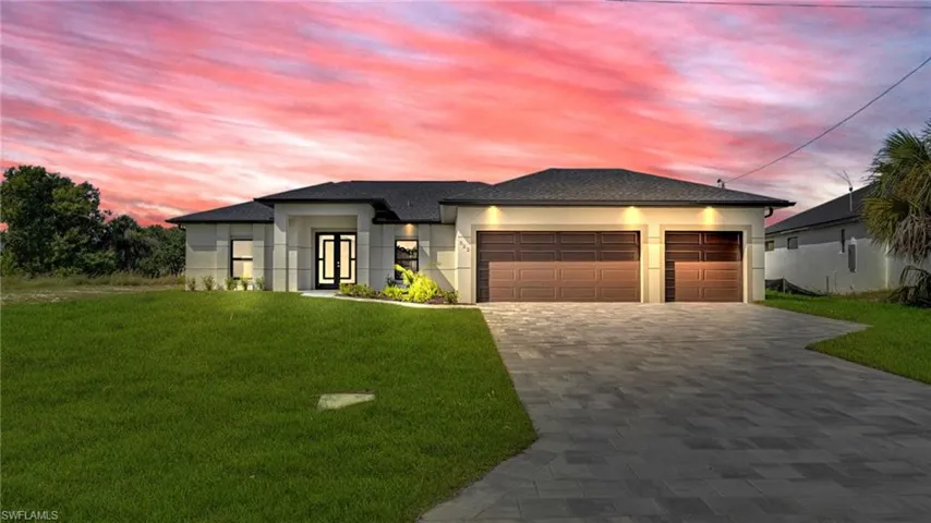 View of front of house with a yard, decorative driveway, a garage, and stucco siding
