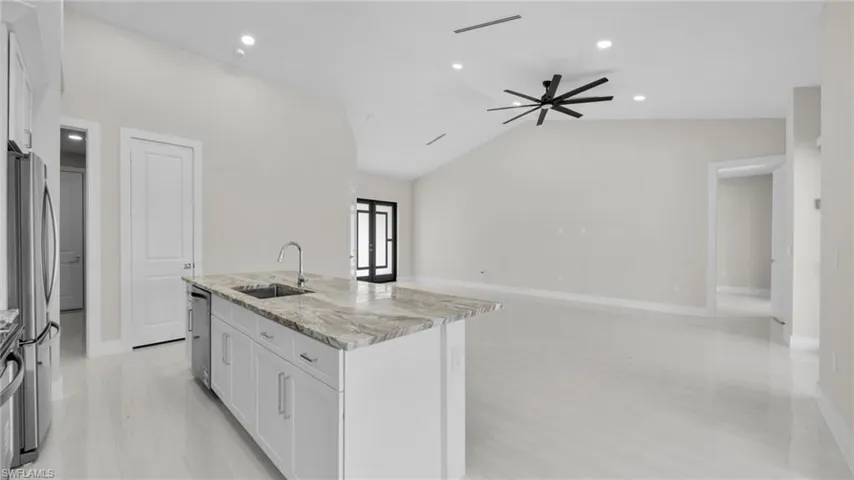 Kitchen featuring light stone counters, white cabinetry, lofted ceiling, a kitchen island with sink, and stainless steel appliances