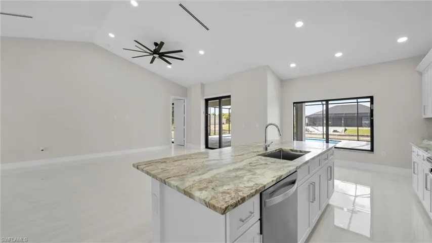 Kitchen with white cabinets, light stone counters, stainless steel dishwasher, a kitchen island with sink, and open floor plan