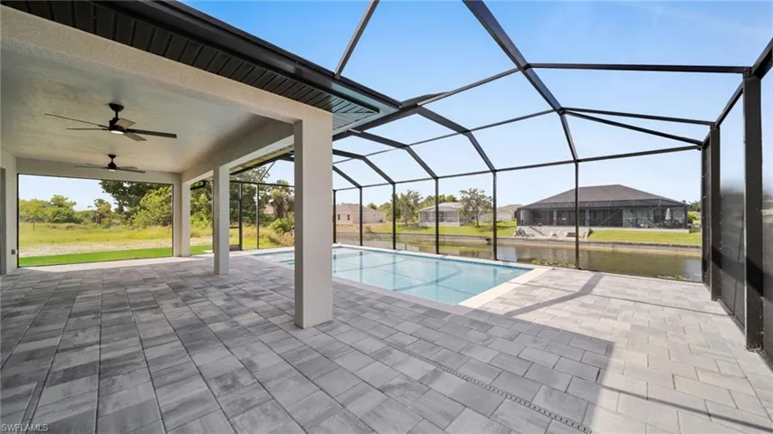 Outdoor pool with ceiling fan, a sunroom, glass enclosure, a water view, and a patio