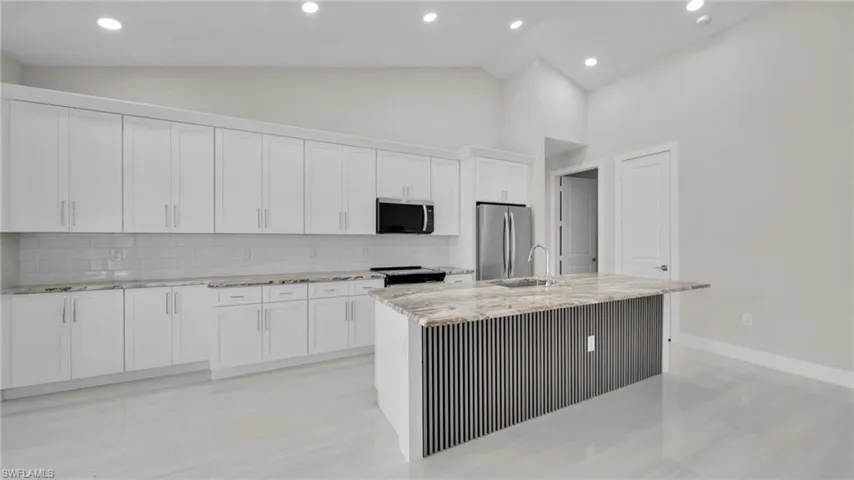 Kitchen with light stone counters, stainless steel appliances, backsplash, a center island with sink, and white cabinetry