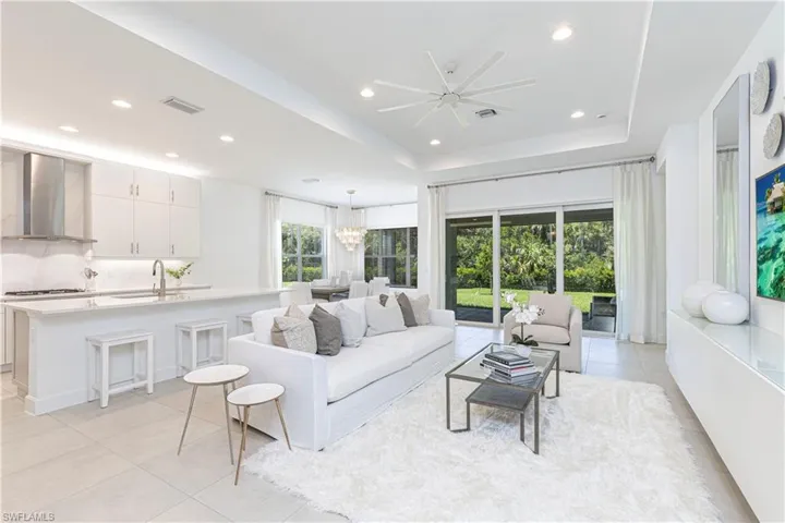 Living room with light tile floors, sink, a raised ceiling, and ceiling fan with notable chandelier