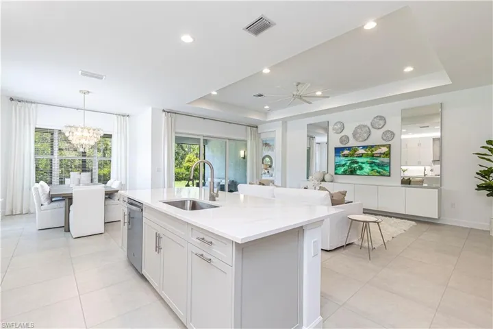 Kitchen with a raised ceiling, an island with sink, sink, and decorative light fixtures