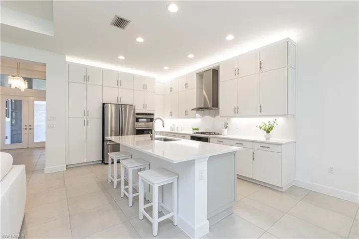 Kitchen with stainless steel appliances, an island with sink, wall chimney exhaust hood, a breakfast bar, and sink