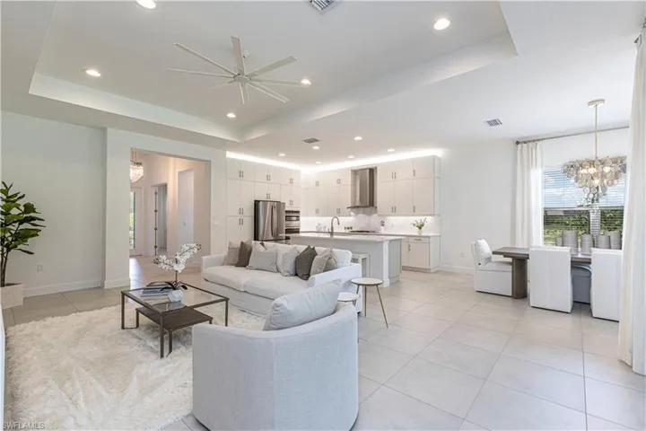 Tiled living room with sink, a tray ceiling, and ceiling fan with notable chandelier