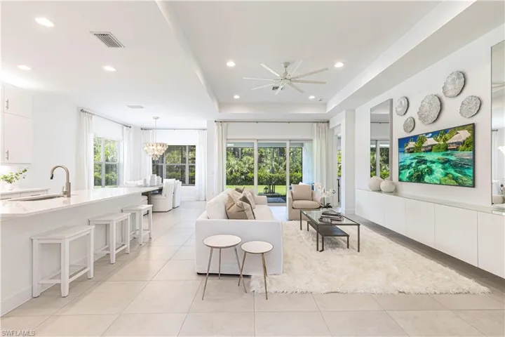 Tiled living room featuring a raised ceiling, sink, ceiling fan with notable chandelier, and a wealth of natural light