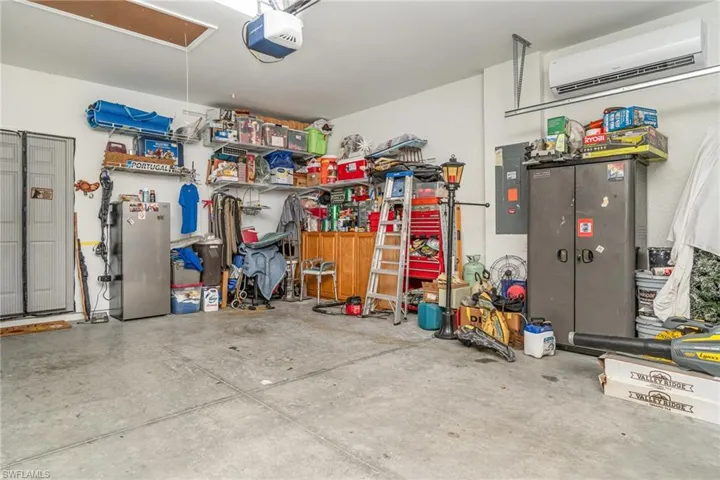 Garage with a wall mounted AC, electric panel, a garage door opener, and freestanding refrigerator
