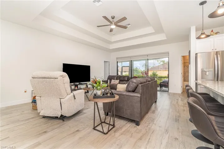 Living area featuring light wood-style floors, a raised ceiling, and a ceiling fan