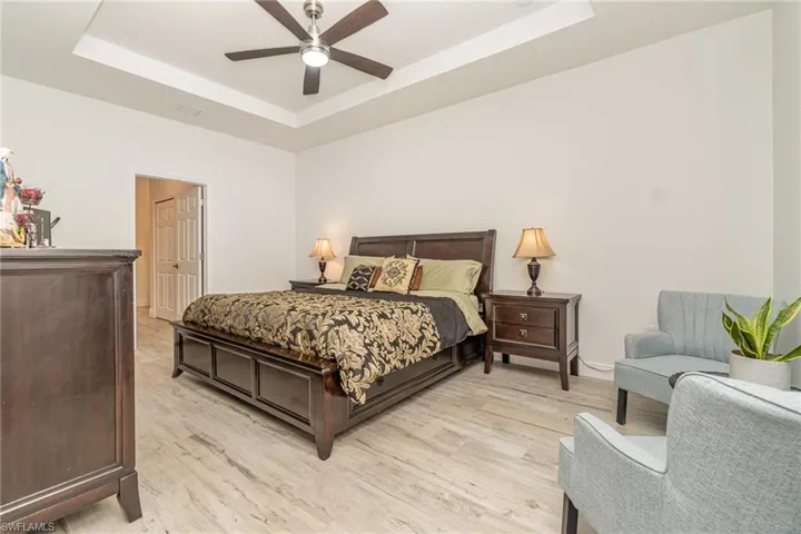 Bedroom with a tray ceiling, light wood-style floors, and a ceiling fan