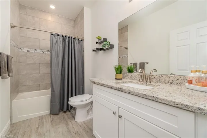 Bathroom with shower / bathtub combination with curtain, vanity, light wood-type flooring, and recessed lighting