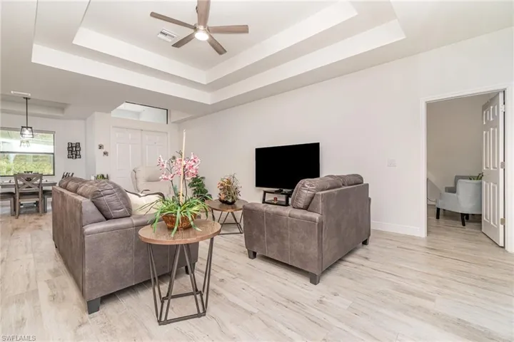 Living room with a tray ceiling, light wood-type flooring, and a ceiling fan