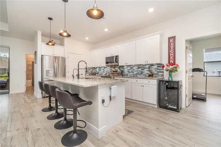 Kitchen featuring a breakfast bar area, white cabinetry, light stone countertops, decorative backsplash, and beverage cooler