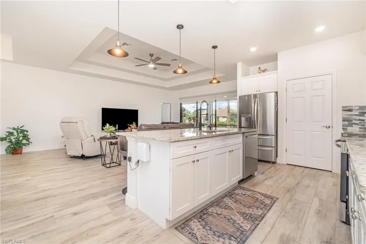 Kitchen featuring white cabinetry, decorative light fixtures, open floor plan, and light stone counters