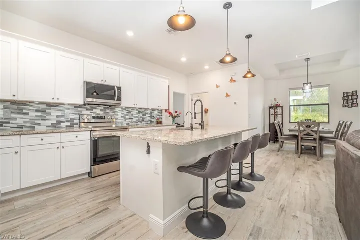 Kitchen featuring appliances with stainless steel finishes, light wood-style flooring, pendant lighting, a kitchen breakfast bar, and white cabinetry