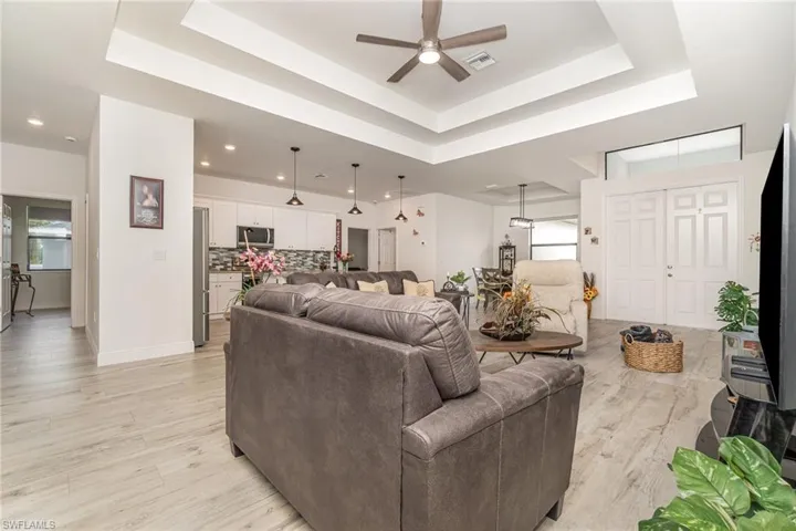Living room featuring a raised ceiling, light wood-type flooring, healthy amount of natural light, and ceiling fan