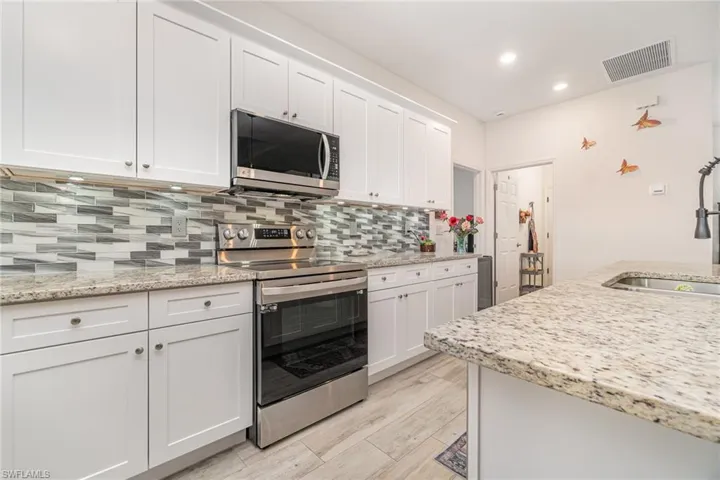 Kitchen with appliances with stainless steel finishes, white cabinets, backsplash, light stone countertops, and recessed lighting