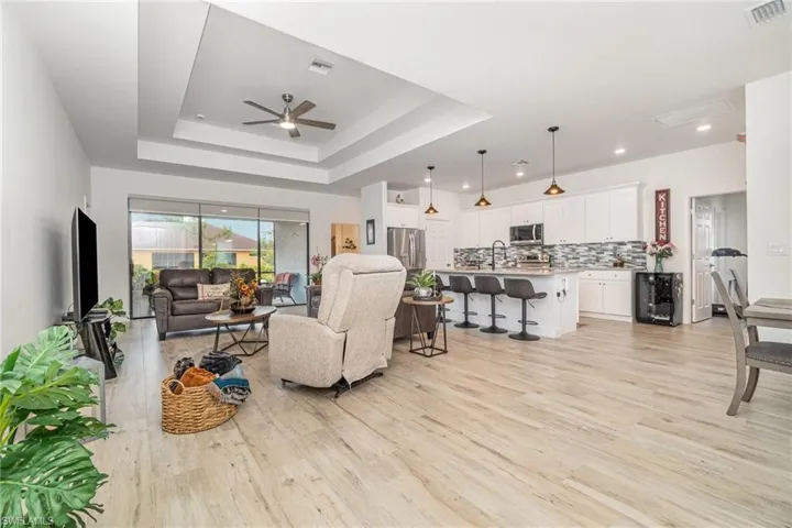 Living area featuring light wood-style floors, a raised ceiling, ceiling fan, and wine cooler