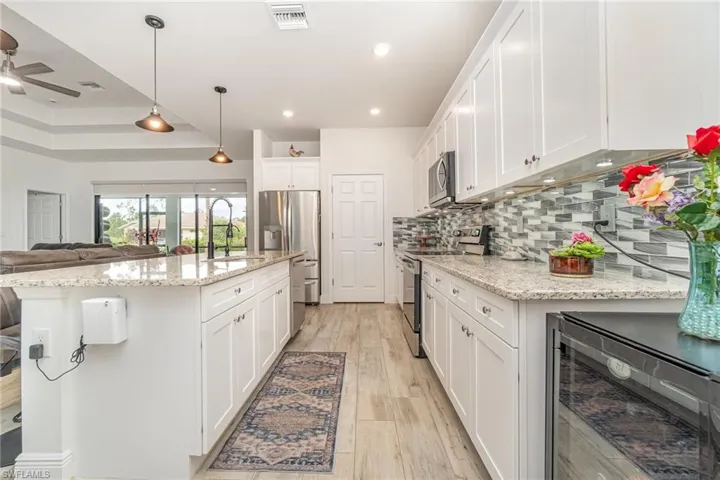 Kitchen with wine cooler, white cabinetry, appliances with stainless steel finishes, open floor plan, and light stone countertops