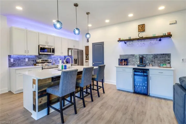 Kitchen with appliances with stainless steel finishes, beverage cooler, pendant lighting, light hardwood / wood-style floors, and white cabinetry