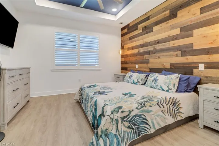 Bedroom with a raised ceiling, wooden walls, light hardwood / wood-style flooring, and ceiling fan