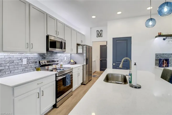 Kitchen with sink, light hardwood / wood-style floors, decorative light fixtures, white cabinets, and appliances with stainless steel finishes