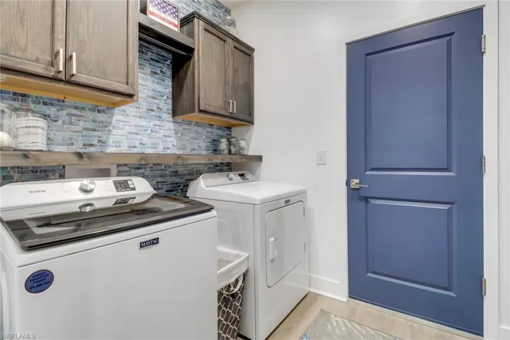Clothes washing area with washing machine and clothes dryer, cabinets, and light hardwood / wood-style floors