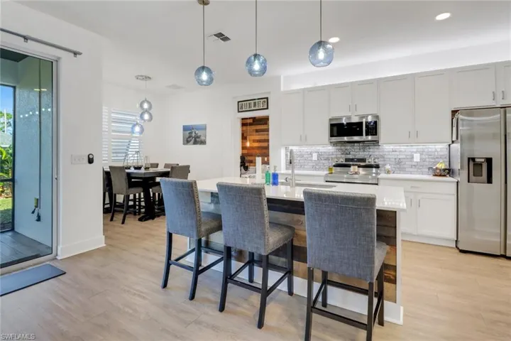 Kitchen with hanging light fixtures, stainless steel appliances, a kitchen island with sink, and light hardwood / wood-style flooring