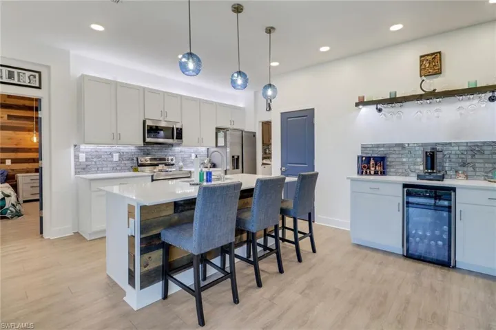 Kitchen featuring hanging light fixtures, wine cooler, light wood-type flooring, an island with sink, and appliances with stainless steel finishes