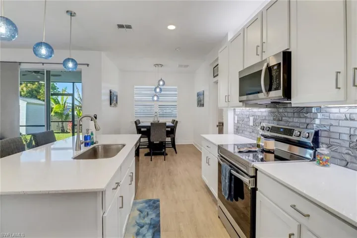 Kitchen featuring appliances with stainless steel finishes, a kitchen island with sink, sink, white cabinetry, and hanging light fixtures